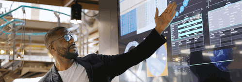 man conducting a seminar / lecture with the aid of a large screen. The screen is displaying graphs & data associated with movie clips of the earth.