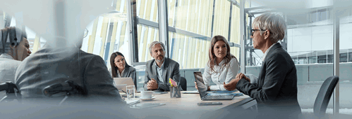Senior Businesswoman Leading A Meeting With Group Of Her Colleagues In The Office. The View Is Through Glass.