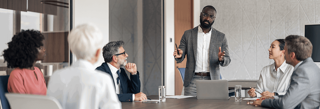 Diverse team of professionals engaging in a corporate meeting, listening intently as a male speaker presents strategy and ideas in a modern office boardroom  3 tags